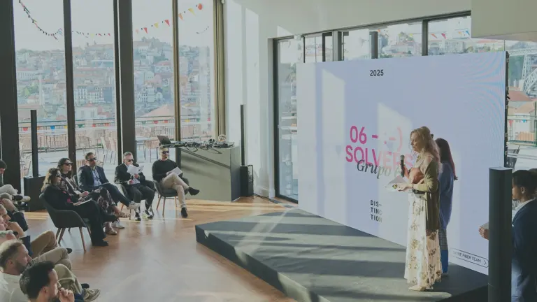 Speaker presenting at conference with audience and skyline.